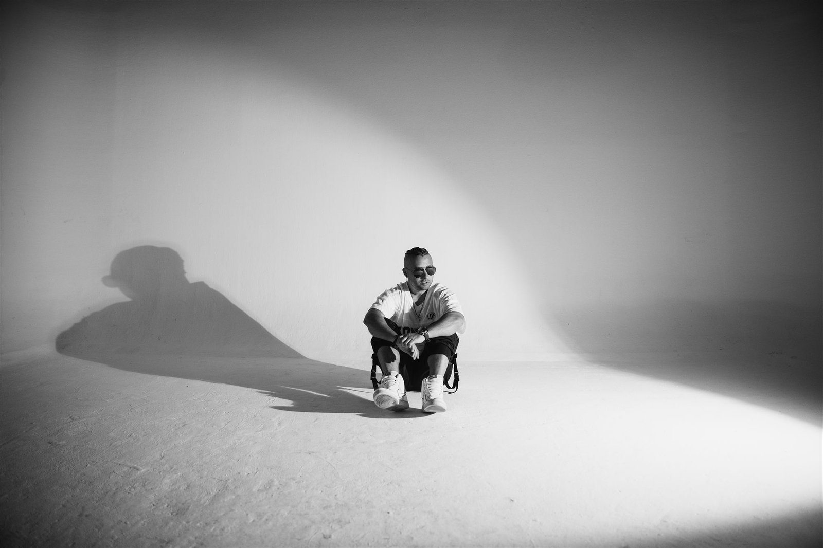 Jembo D. sentado en el piso bajo un haz de luz, blanco y negro